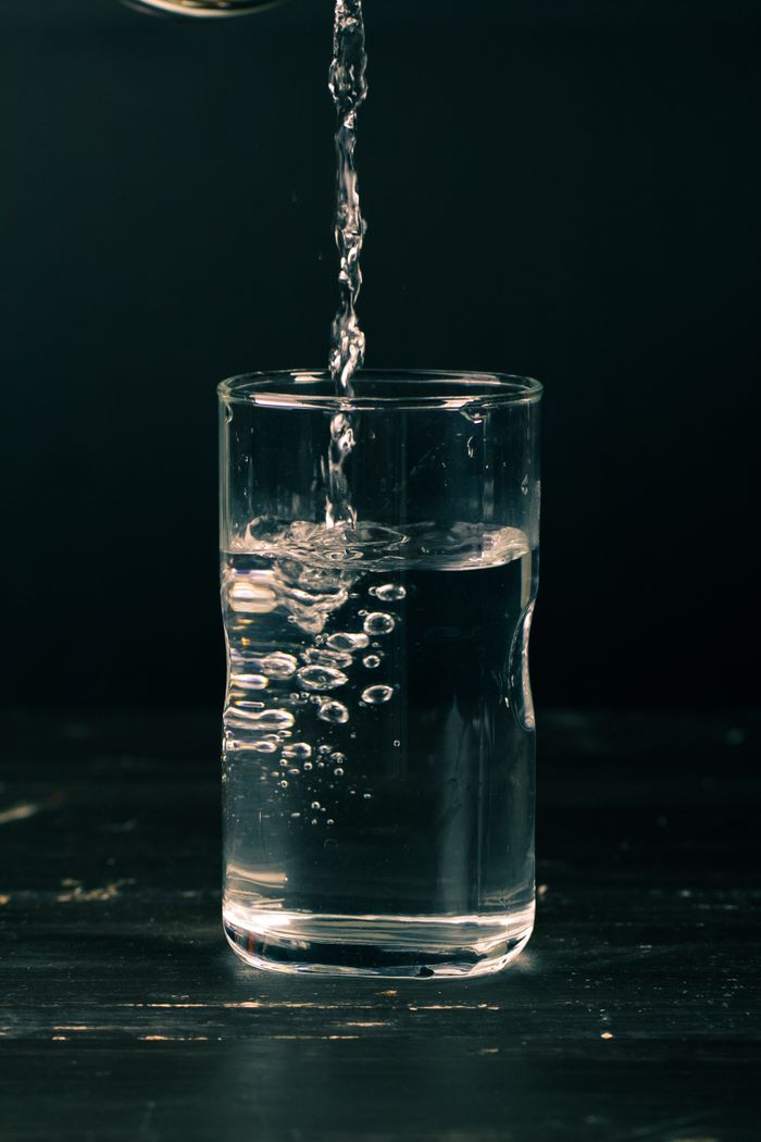 Clear water being poured into a glass with visible bubbles, dark background, refreshing feel.