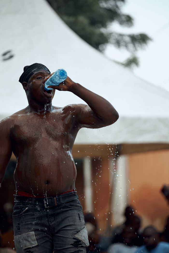 A muscular man pours water over himself to cool down during an outdoor event.