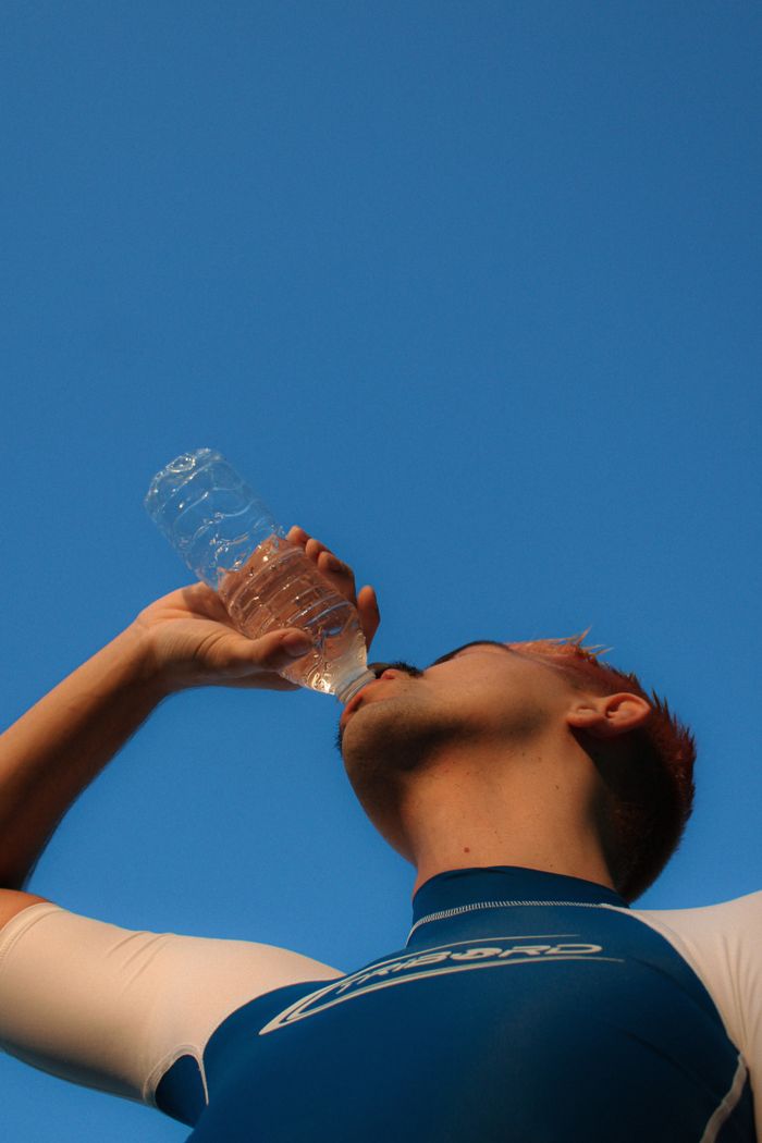 From below of anonymous male athlete in sportswear with mustache standing against cloudless sky while drinking water from plastic bottle